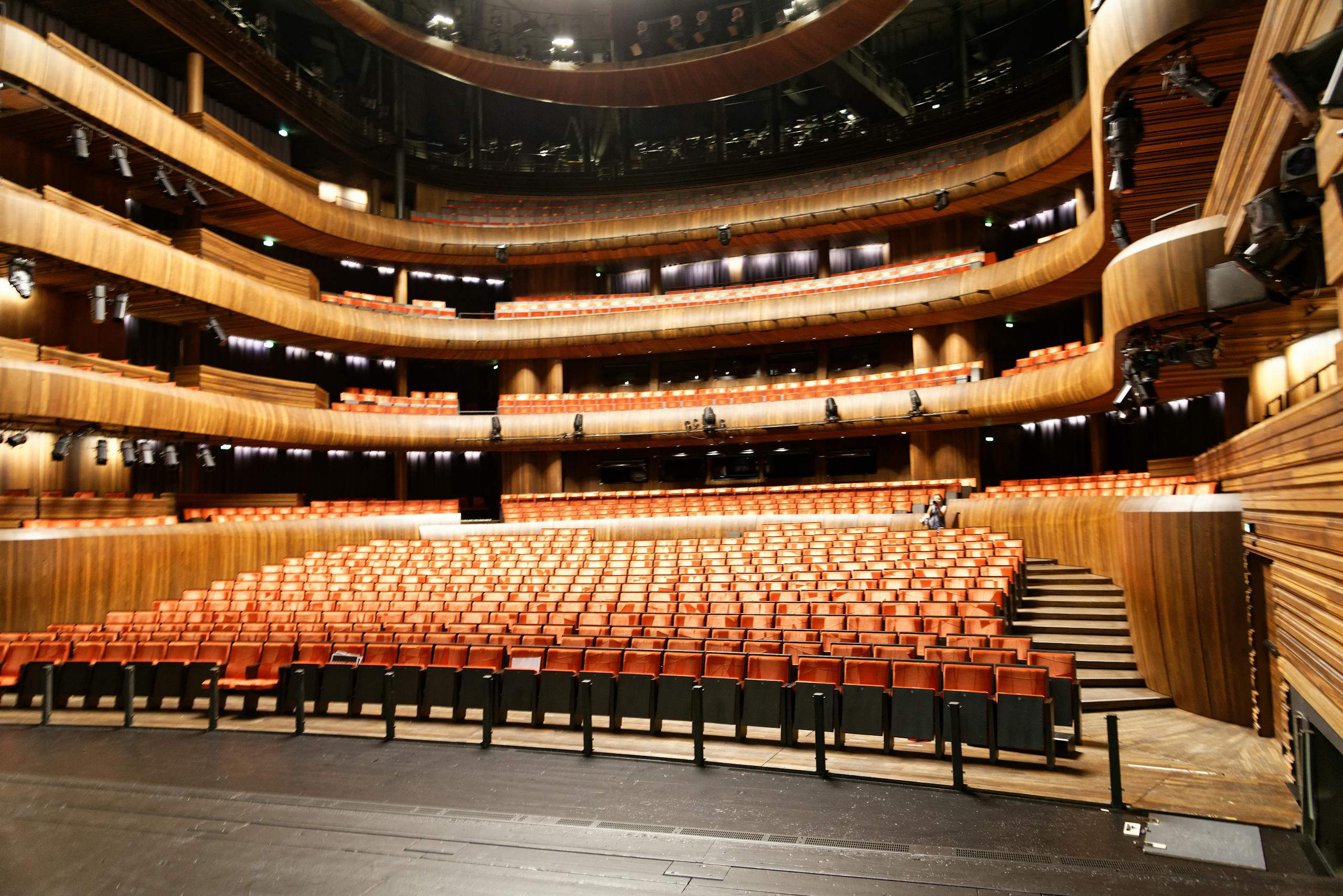 A spacious and modern indoor theatre featuring wooden interior and illuminated seating.